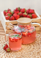 Close-up juicy berry drink from ripe strawberry in glass cup and teapot on table