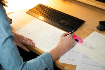 Naklejka premium Sketch of wireframe for website. Women designer working on a mobile application, drawing on paper.