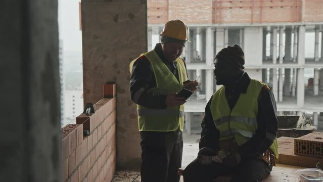 Ethnically diverse construction workers wearing uniform eating lunch and watching funny photos on smartphone