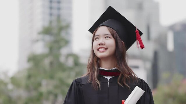 Successful graduation from university. Smiling beautiful Asian girl university or college graduate standing over university at background.