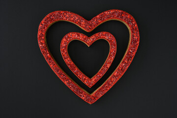 Two glittery red heart shapes on a black background, happy Valentine’s Day
