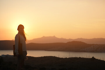 Silhouette of a girl at sunset, person stands on a hill against the backdrop of the sea at dawn, sunrise