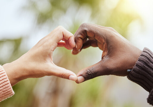 Love, a couple and heart hand sign with nature, man and woman together with affection and diversity. Marriage, heart hands and a celebration of multiracial relationship with support and trust in park