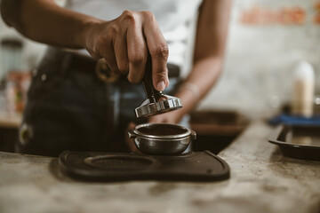 Barista using a tamper to press ground coffee into a portafilter. Coffee maker concept..