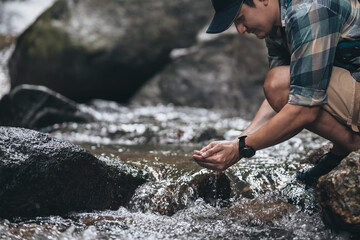 Hikers hand holding transparent clear water from waterfall with backpacks on the rock and water on stream in the forest. hiking and adventure concept.