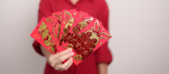 Woman holding Chinese red envelope with golden rabbit and blessing word, money gift for happy Lunar New Year holiday. Chinese sentence means happiness, healthy, Lucky and Wealthy
