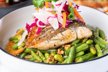 A close view of grilled barramundi with green beans in a round white bowl