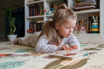 Little cute girl reading a book in the room, soft focus background. Education at home concept. 