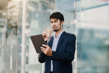 Fototapeta premium Young Happy Businessman using tablet. Stylish young Manager Smiling, Working on Financial and Marketing Projects. Drinking Coffee from a Mug.