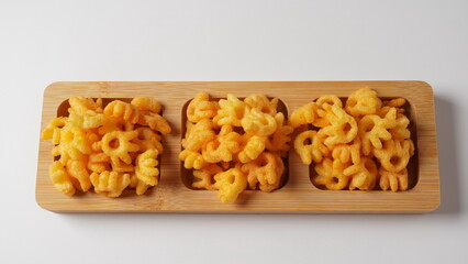 Cheetos is a crunchy corn puff snack. Bright orange cheese puffs in a wooden board.
