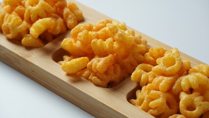 Cheetos is a crunchy corn puff snack. Bright orange cheese puffs in a wooden board. - obrazy, fototapety, plakaty