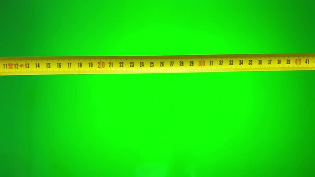 Female hands in the frame on a green chromakey background are measured with a yellow centimeter Top View Close Up Of Man's Hands With Measuring Ruler On green Background. High quality 4k footage