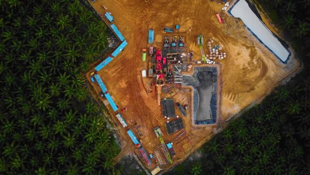 Cinematic 4K Drone Footage of Onshore Drilling Rig equipment structure for oil exploration and exploitation in the middle of jungle surrounded by palm oil trees during sunset and high oil price.