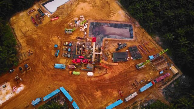 Cinematic 4K Drone Footage of Onshore Drilling Rig equipment structure for oil exploration and exploitation in the middle of jungle surrounded by palm oil trees during sunset and high oil price.