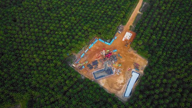 Cinematic 4K Drone Footage of Onshore Drilling Rig equipment structure for oil exploration and exploitation in the middle of jungle surrounded by palm oil trees during sunset and high oil price.