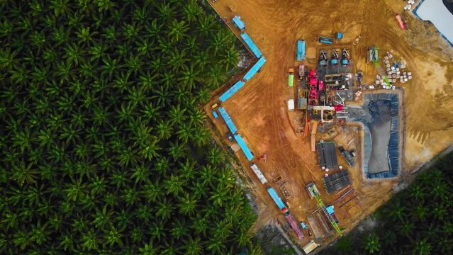 Cinematic 4K Drone Footage of Onshore Drilling Rig equipment structure for oil exploration and exploitation in the middle of jungle surrounded by palm oil trees during sunset and high oil price.