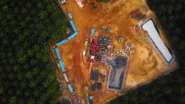 Cinematic 4K Drone Footage of Onshore Drilling Rig equipment structure for oil exploration and exploitation in the middle of jungle surrounded by palm oil trees during sunset and high oil price.