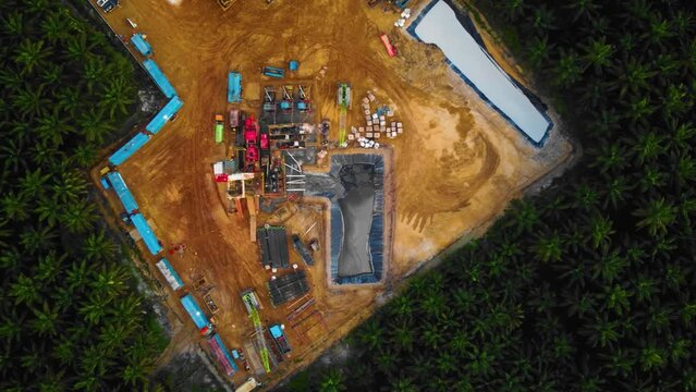Cinematic 4K Drone Footage of Onshore Drilling Rig equipment structure for oil exploration and exploitation in the middle of jungle surrounded by palm oil trees during sunset and high oil price.