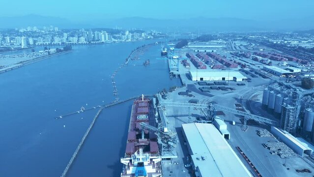 grain loading on freighter from distribution port canal in Surrey BC Canada top birds eye view overlooking commercial dock as other cargo ship are getting loaded with wood vehicles drone flyover 1-2