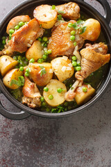 Chicken Vesuvio is a classic Italian-American dish for baked chicken with potatoes, peas, white wine sauce, and seasonings close-up in a frying pan on the table. Vertical top view from above