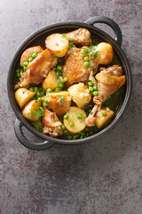 Delicious pieces of chicken cooked with potatoes and green peas close-up in a frying pan on the table. Vertical top view from above