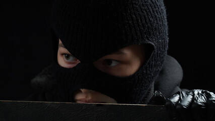 Masked female burglar in black gloves looks over a fence. Crime concept
