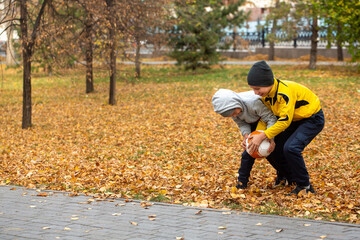 Full contact. Two boys trying to take a soccer ball from each other in the park outdoor in golden autumn, selective focus.