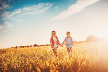 Fototapeta na wymiar Two children running on the summer field by holding hands.