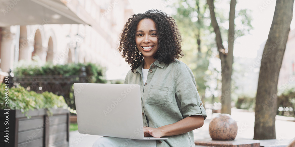 Sticker Young beautiful woman using laptop computer in a city panoramic banner. Smiling student girl typing laptop outdoor. Modern lifestyle, connection, online business, freelance concept