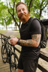 Young handsome smiling tattooed bearded man holding phone looking aside