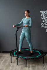 fitness woman in sportswear poses on sports trampoline in the gym against gray wall background.