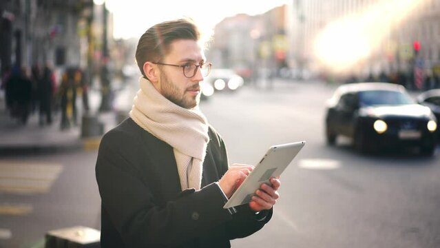 Man modern artist or designer stands in city center on busy street with cars, looks at interior of historic building and draws using graphics tablet. Inspiration and creativity outdoors. Hobby, work.