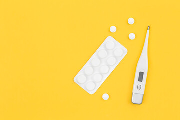 Pills and electronic thermometer on a yellow background, flat lay.