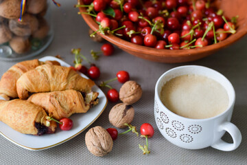 Breakfast on the table with coffee, cherries, nuts and croissants, good morning mood.