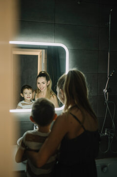 Happy mother and son standing in front of mirror at home