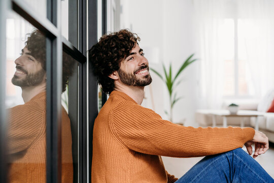 Thoughtful young man leaning on glass door at home