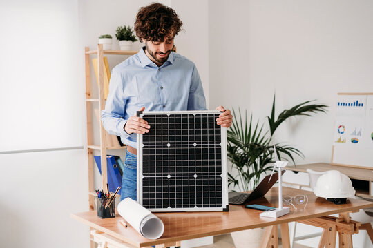 Young businessman holding solar panel at desk in office