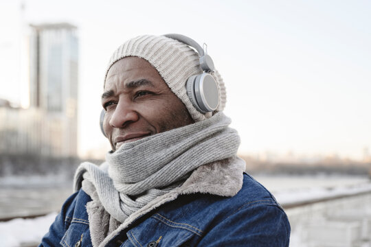 Smiling man wearing warm clothing enjoying music through wireless headphones