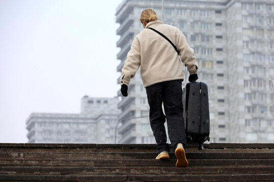 City travel in winter, woman goes up the street stairs with suitcase in snow weather