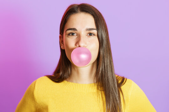 Young woman blowing bubble gum against purple background