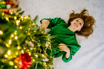 Happy girl lying on carpet under illuminated Christmas tree at home