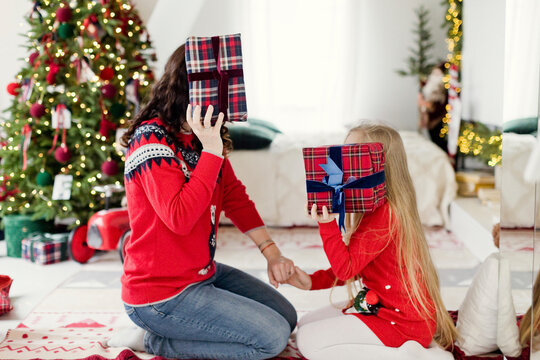 Mother and daughter covering face with gifts at home