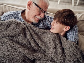 Grandfather and son snuggling under a blanket on couch in living room