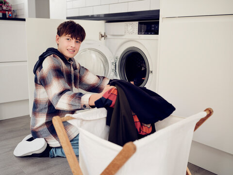 Smiling boy putting laundry into washing machine at home