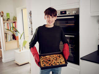 Portrait of boy holding baking tray with fresh focaccia bread in the kitchen