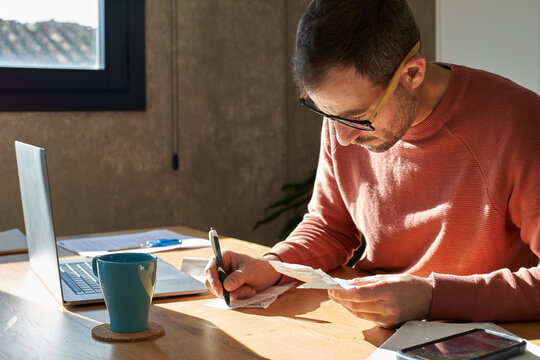 Man writing with pen and examining financial bills at home