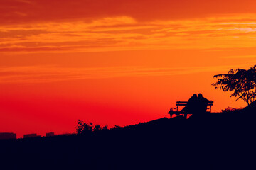 Silhouette of two young males sitting on a bench in sunset close to each other, rear view