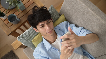 top angle view of a sleepy Korean guy dropping his cell phone while lying on the couch and browsing...