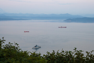 Fototapeta na wymiar Ships on the roadstead in the bay. View of cargo ships and a large yacht. Mountains in the distance. Avacha Bay, Petropavlovsk-Kamchatsky, Kamchatka Territory, Far East of Russia. Blurred foreground.