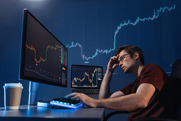 Crypto trader investor looking at computer screen with candlestick chart late night, thinking about...